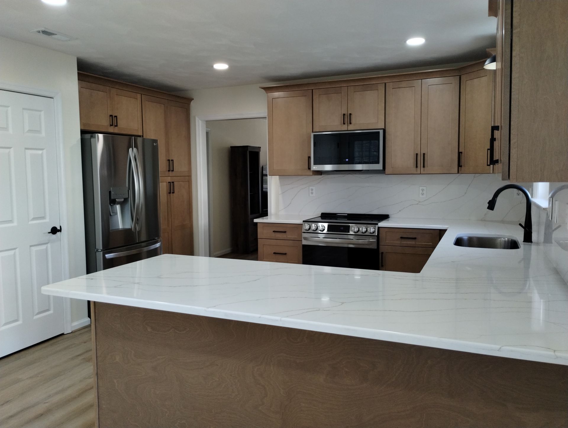 Modern kitchen with light wood cabinets, stainless steel appliances, and white countertops.