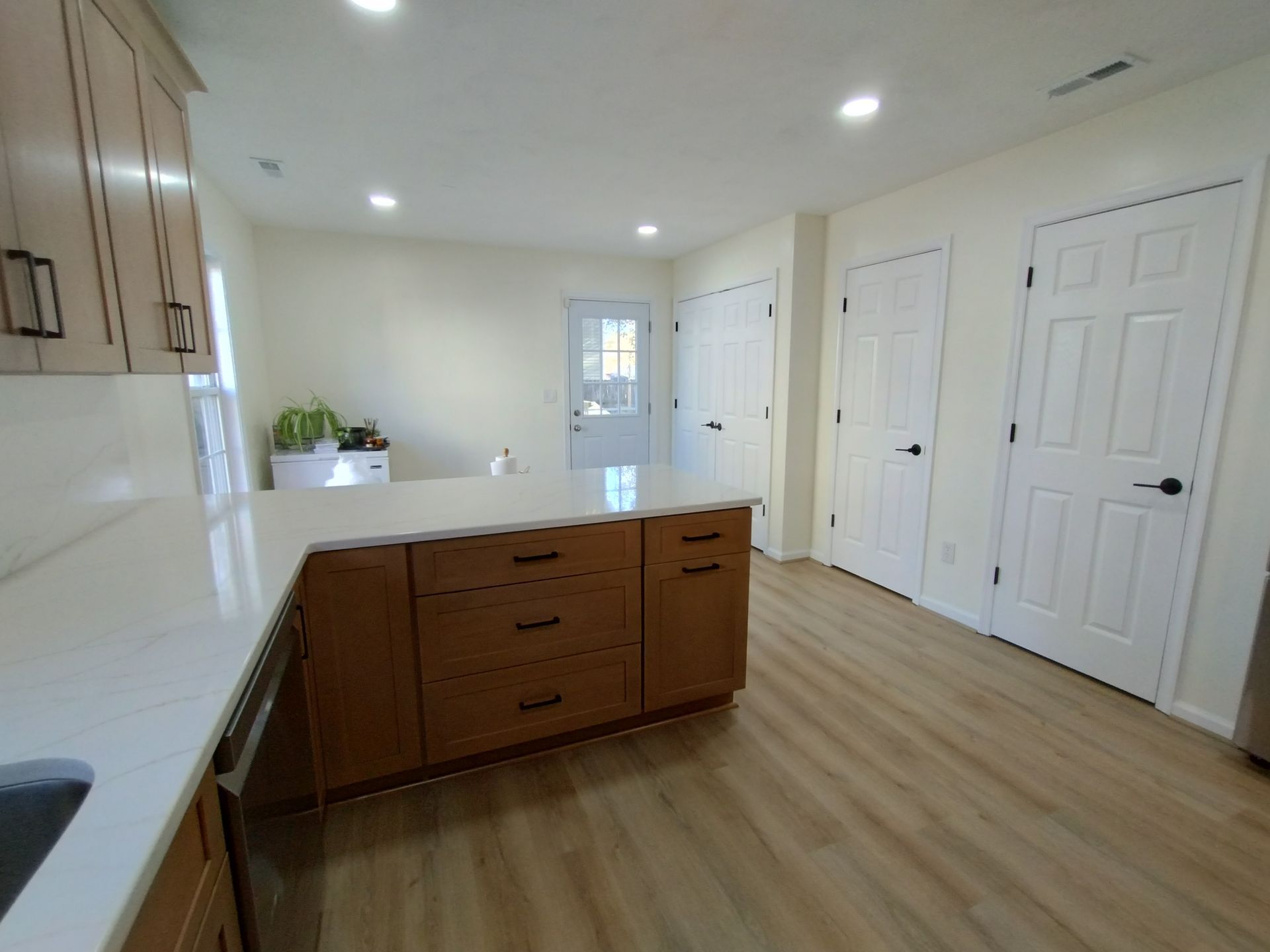 Bright kitchen with island, light wood cabinets, white countertops, light floors, and white walls.