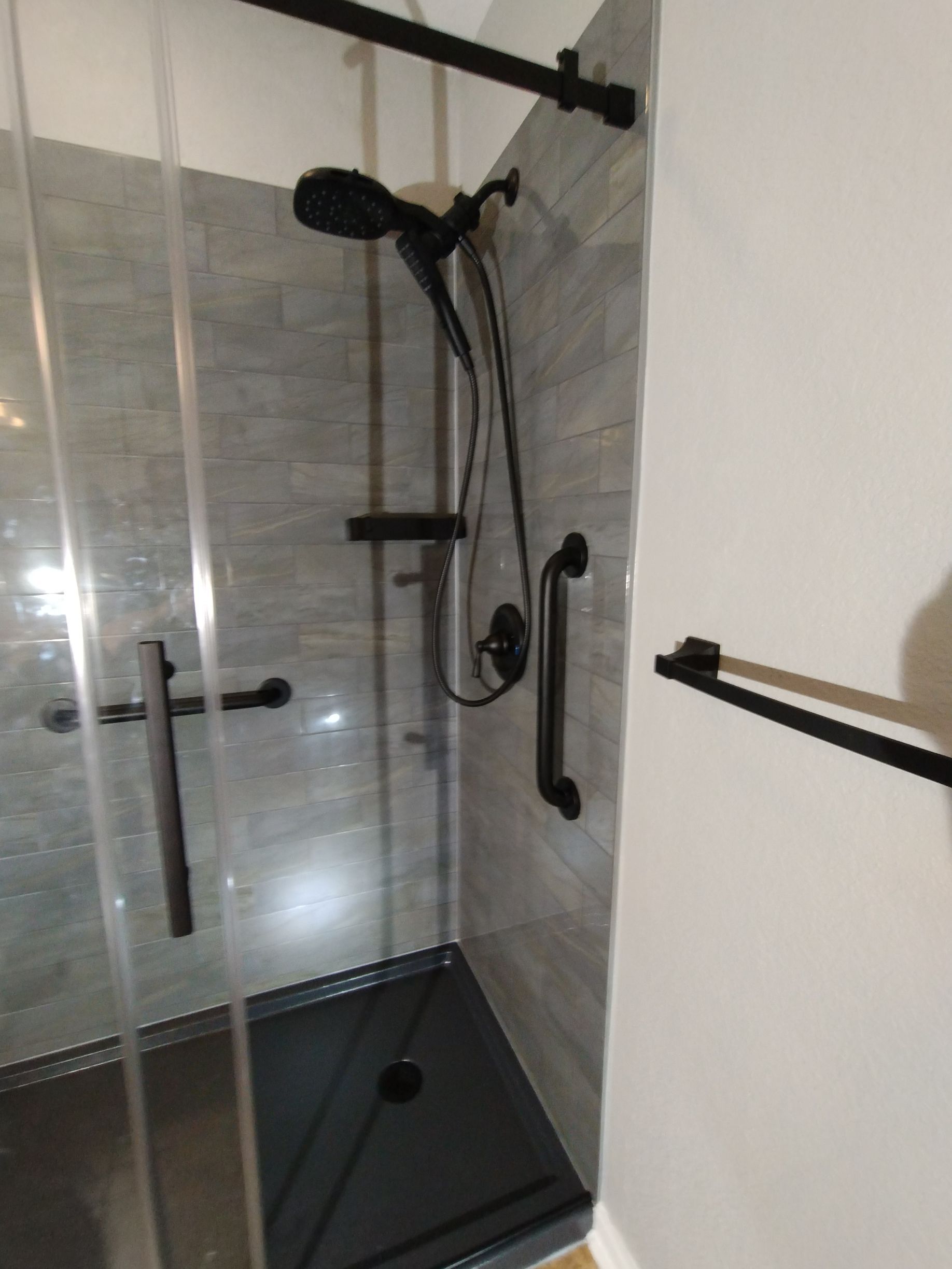 A modern bathroom shower stall with gray tile, black fixtures, and a glass door.