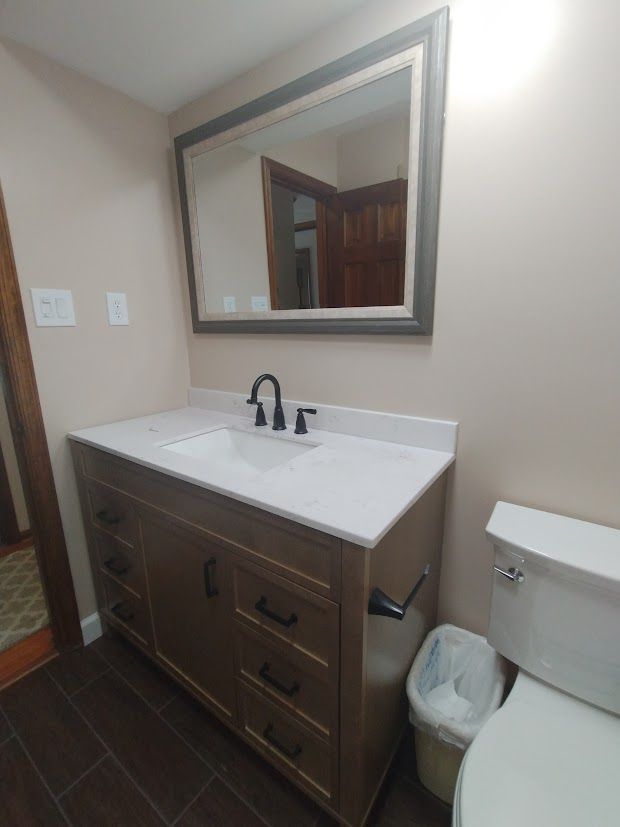 Bathroom with a wooden vanity, white countertop, black faucet, and large mirror.