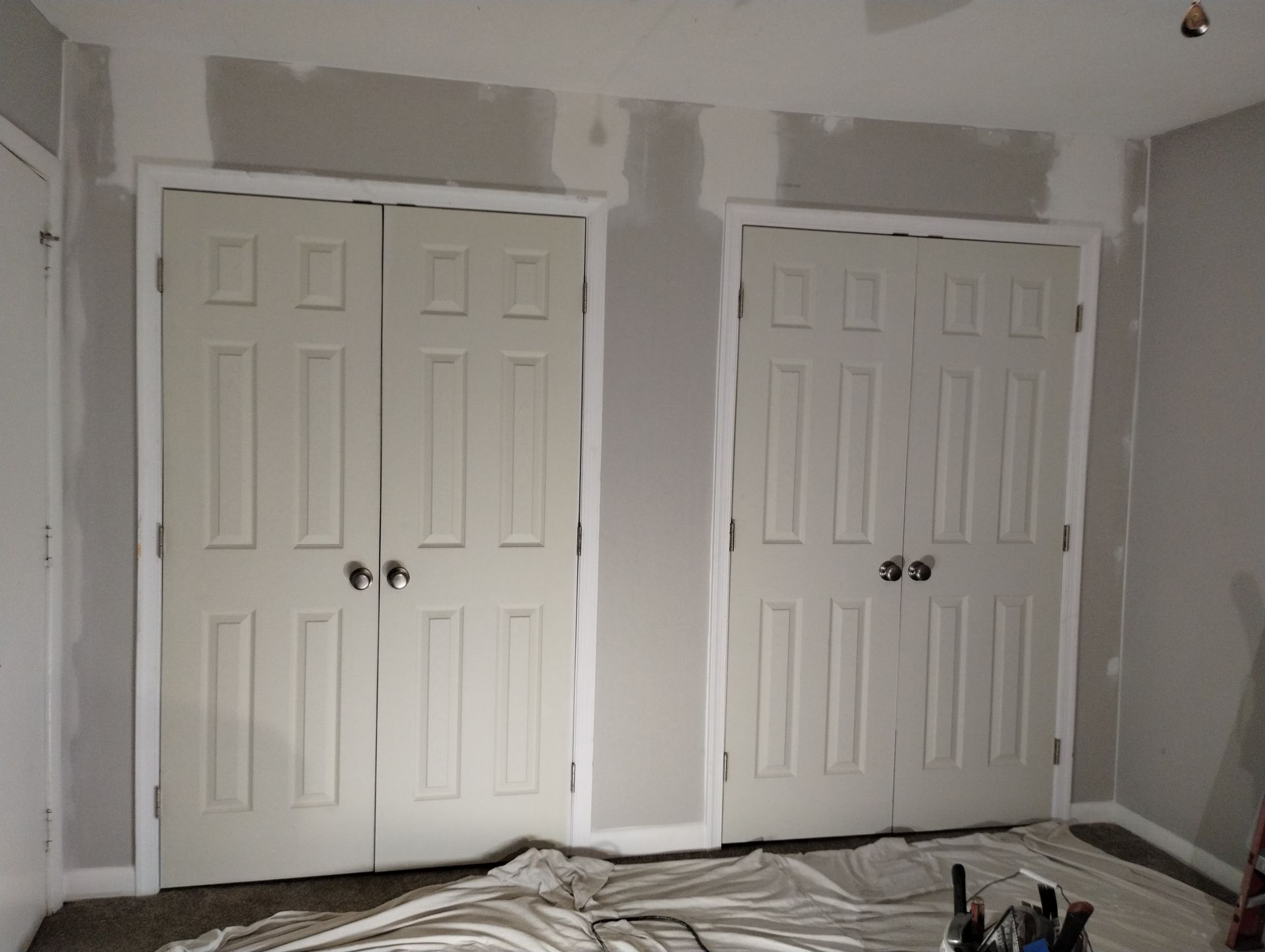 Two beige closet doors with white trim, gray walls, and paint tarps on the floor.