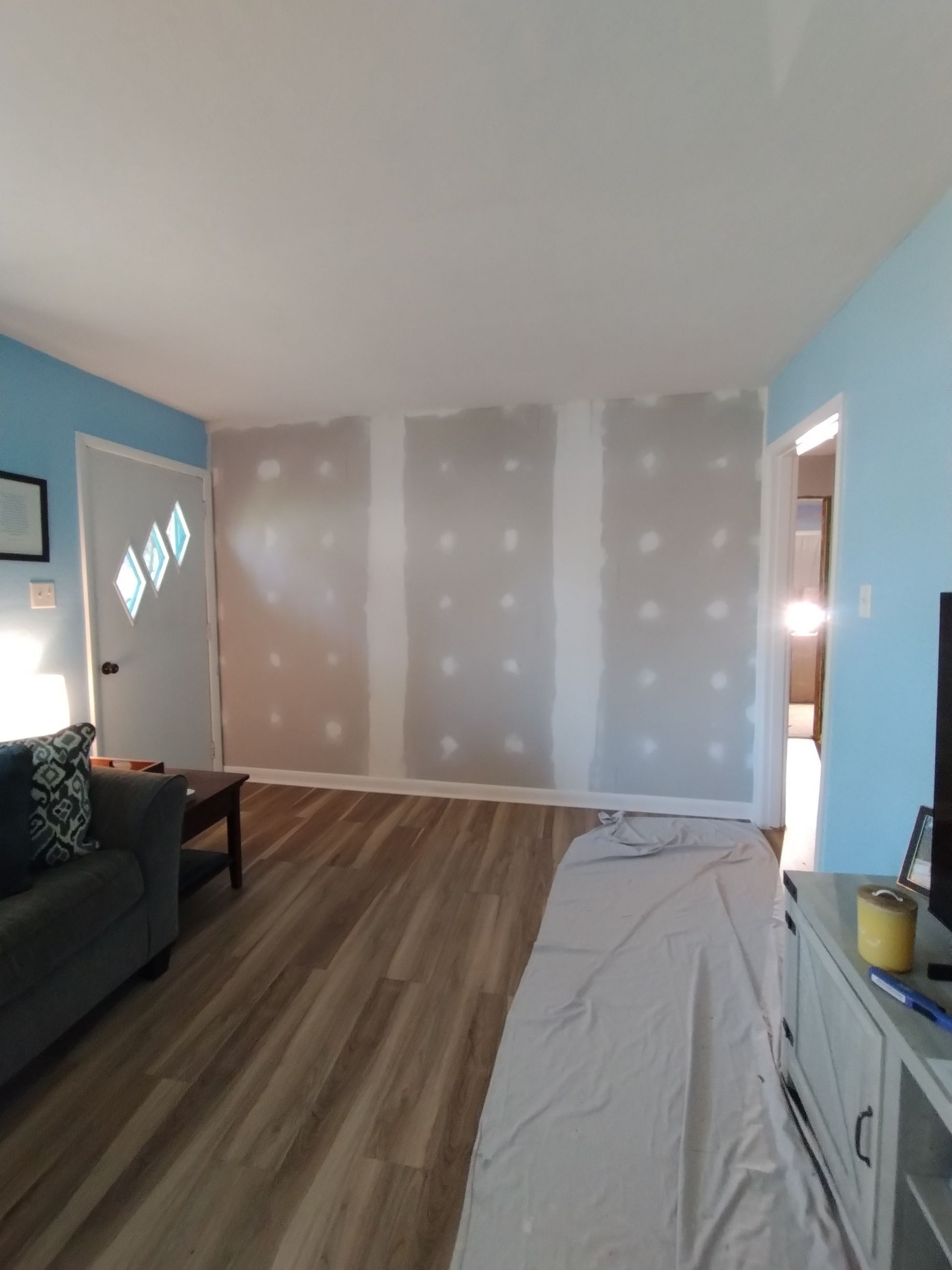 Interior view of a living room with three drywall sections; blue walls, hardwood floor, a sofa, and a door.