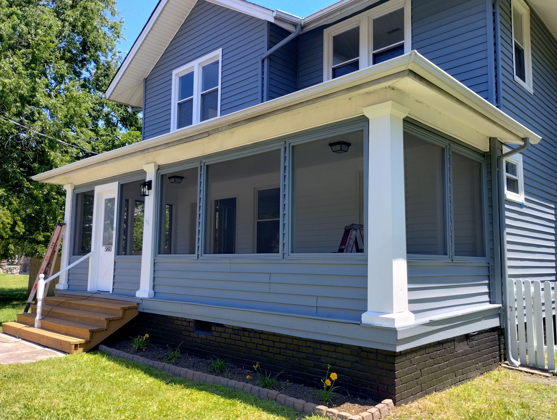 Blue house with screened porch and white columns, wooden steps, and green grass.
