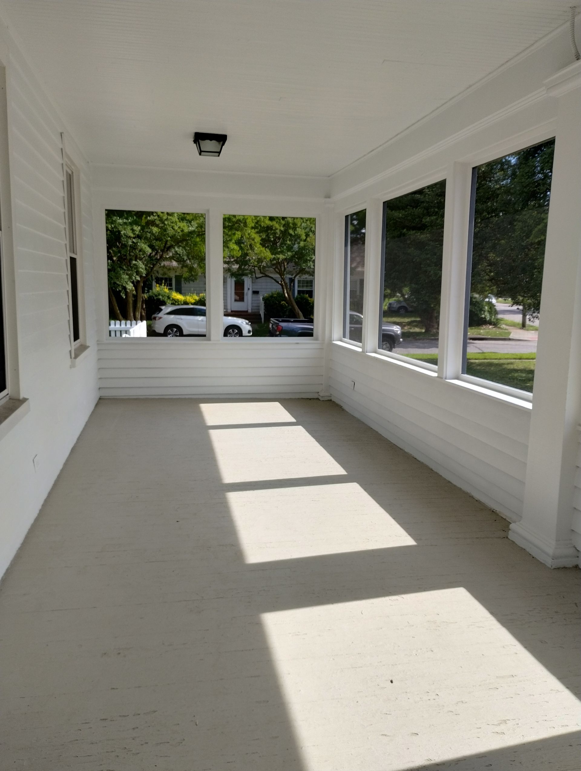 White porch with multiple windows, sunlight, and a gray floor.