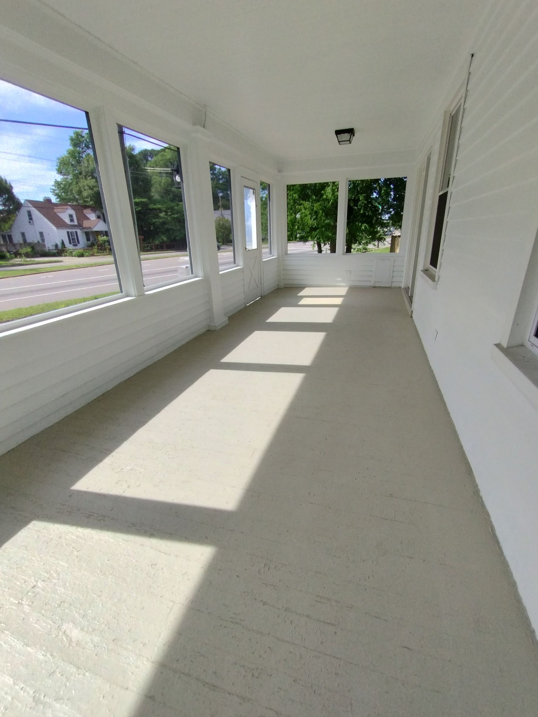 White porch with long windows, sunlight, and a gray floor.