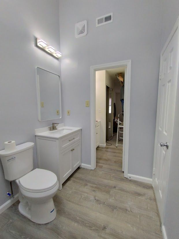 Bathroom with a white toilet, sink, and door. Light gray walls and flooring.