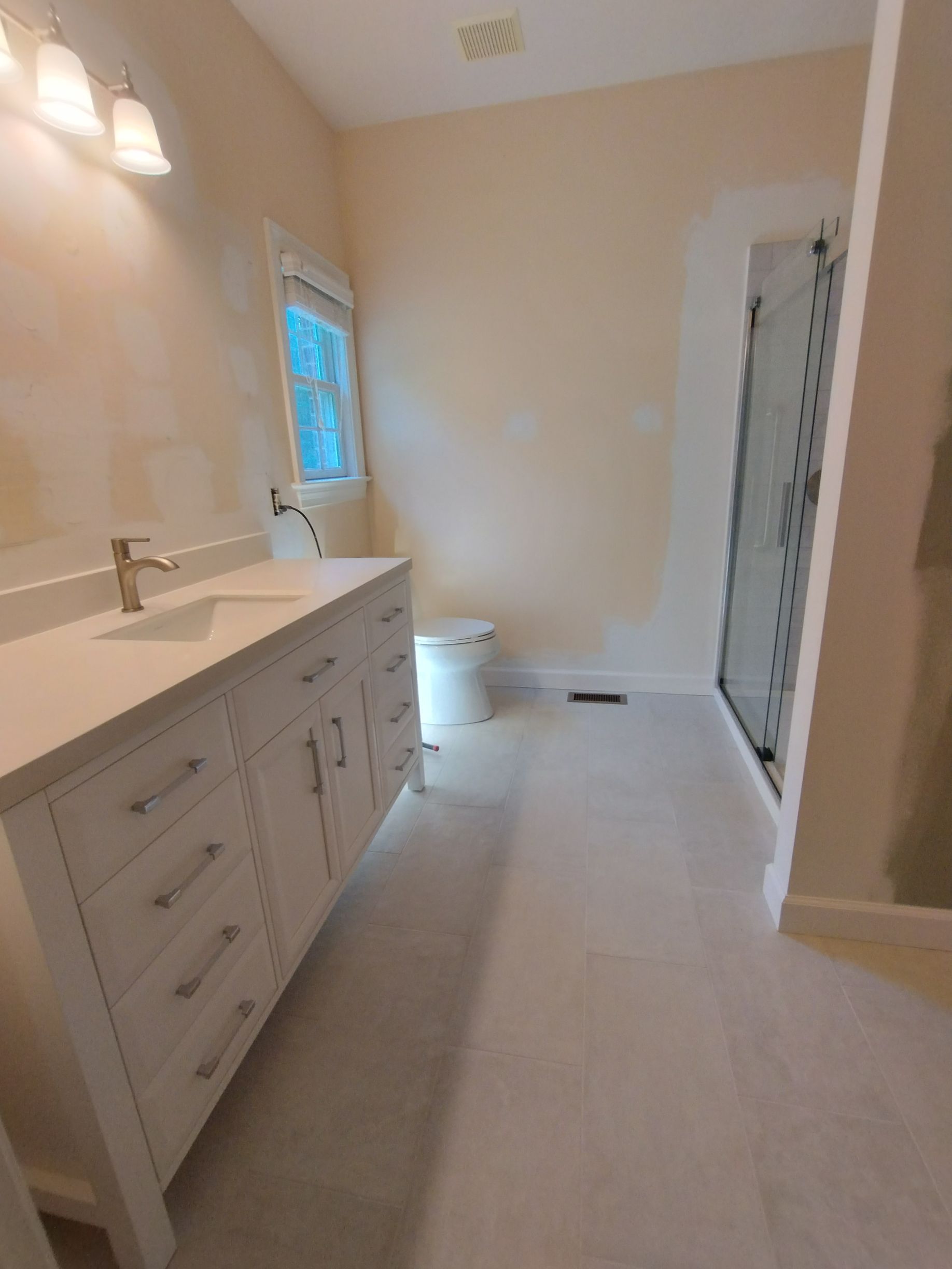 Bathroom with white vanity, toilet, and shower. Light-colored walls and floors.