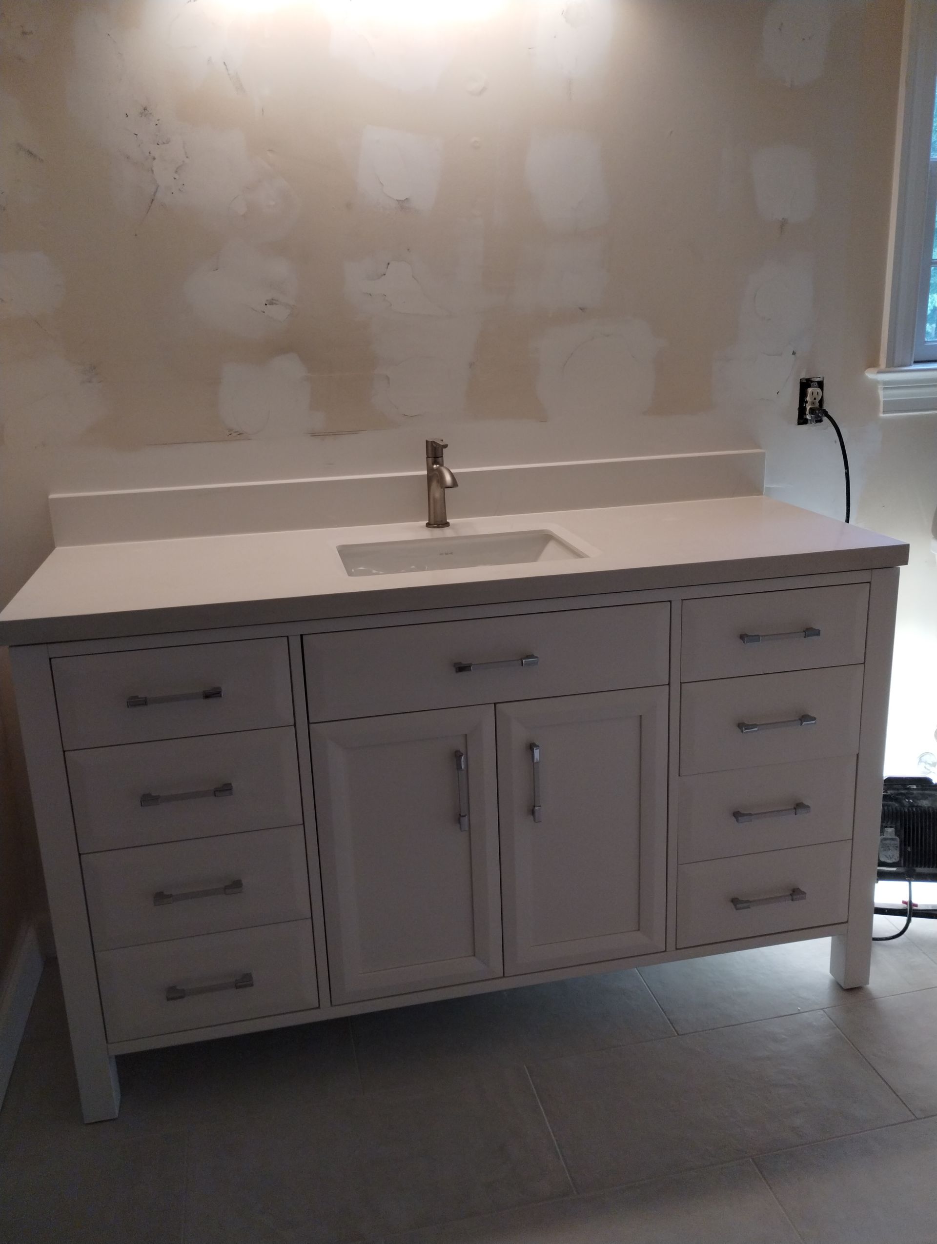 White bathroom vanity with a light countertop against a patchy wall.