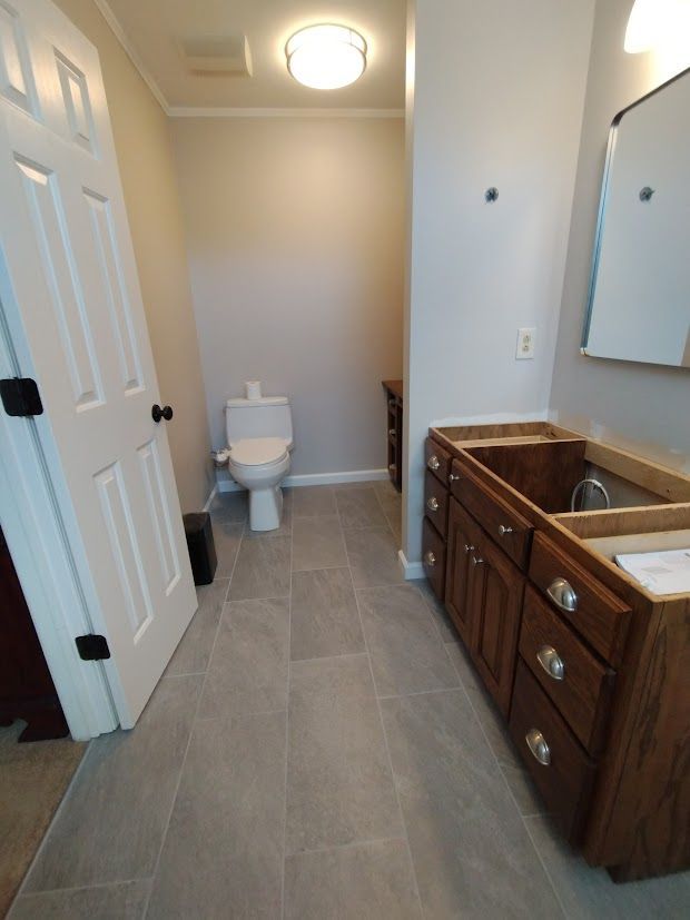 Bathroom renovation with new gray tile floor, toilet, vanity, and door.