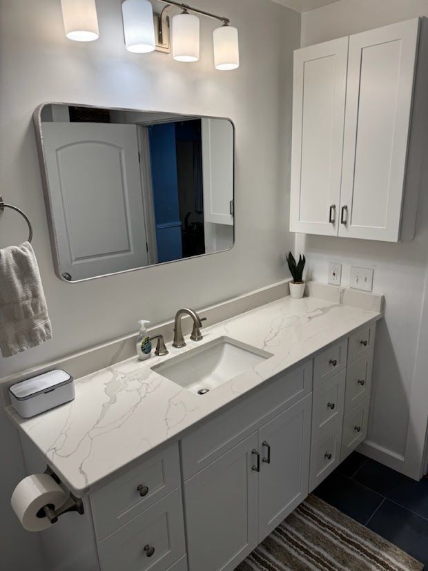 White bathroom with vanity, mirror, and cabinet. Light countertops. Silver fixtures.