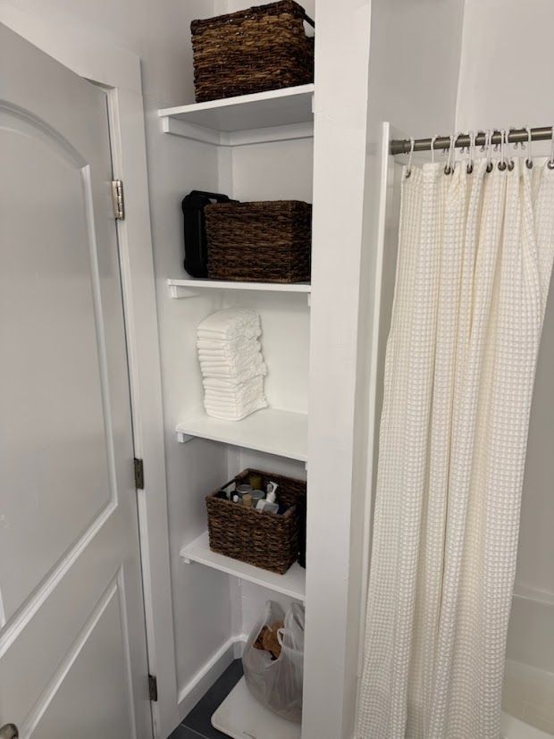 White bathroom storage cabinet with baskets, holding toiletries and towels.