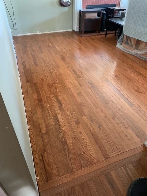 Newly refinished hardwood floor in a room, with a step down. Light brown stain with glossy finish.