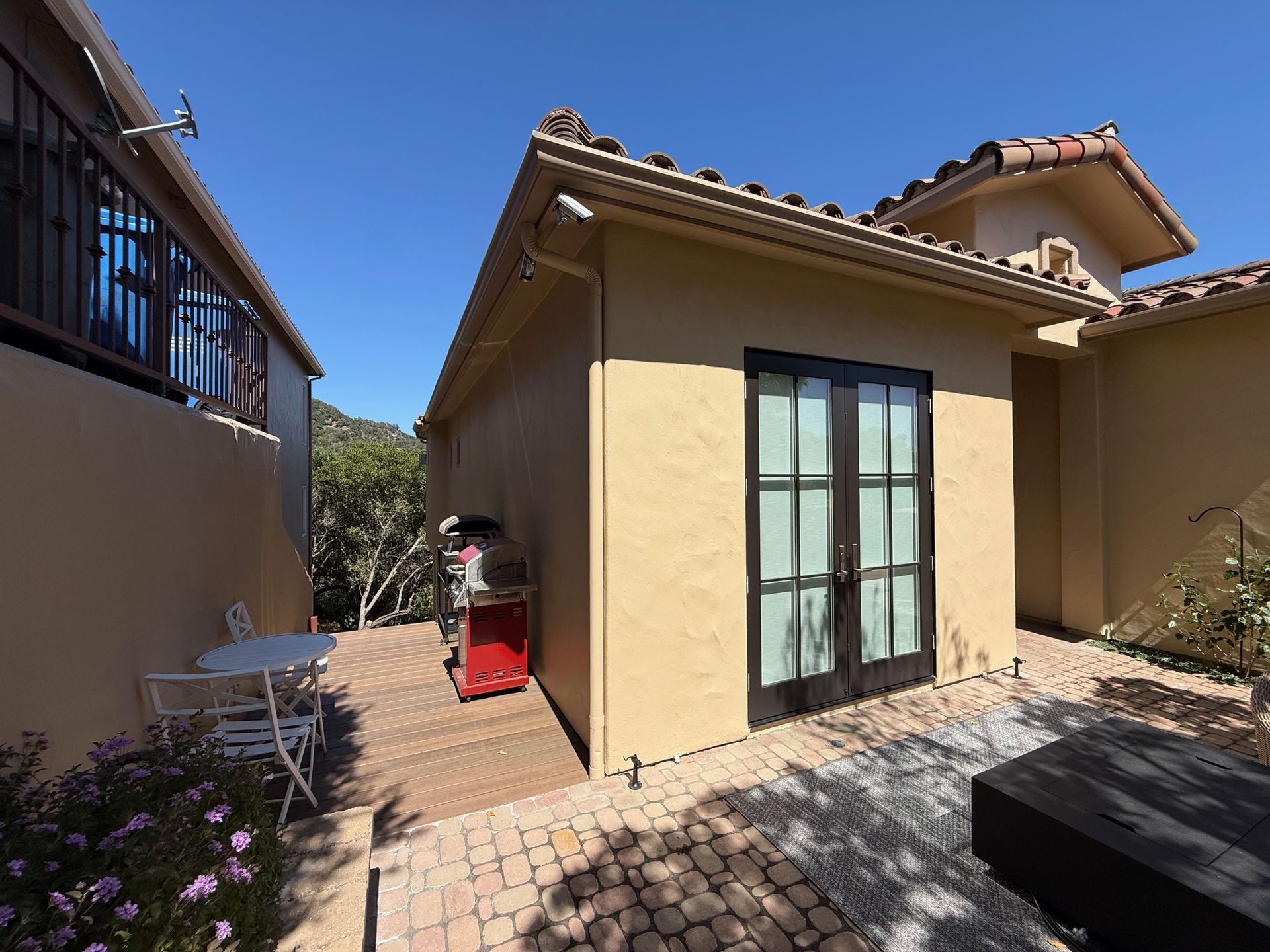Exterior of a stucco building with a black-framed double door, next to a seating area and walkway; sunny day.