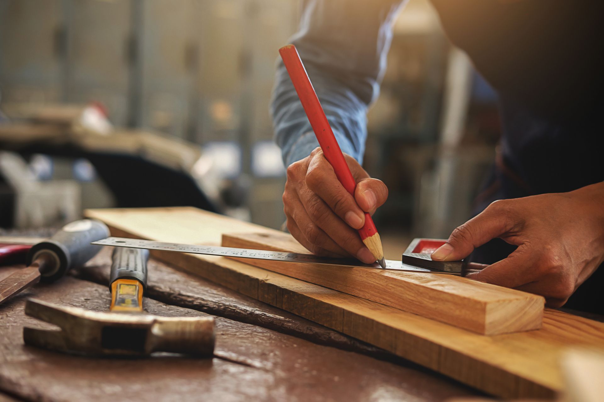Person using a pencil, ruler, and square to measure and mark a wooden plank in a workshop.
