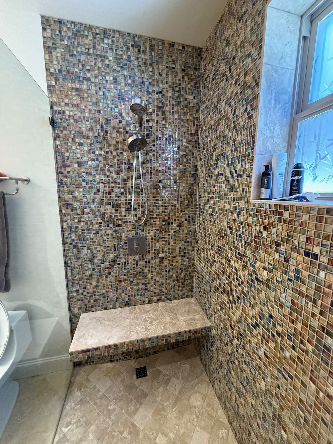 A bathroom with a walk in shower with a bench and a window.