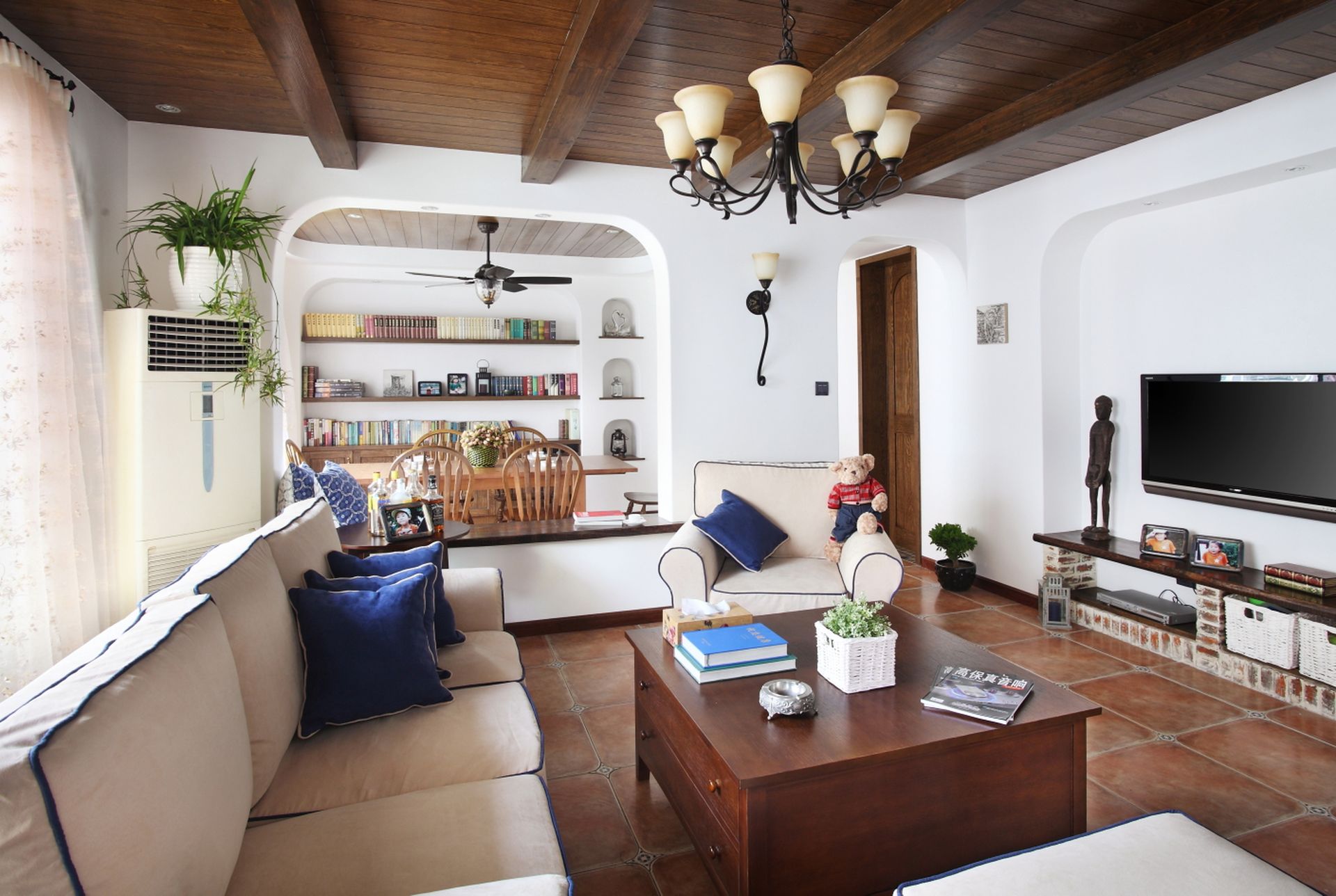 Cozy living room with beige sofas, wooden coffee table, bookcase, TV, and terracotta tile floor.