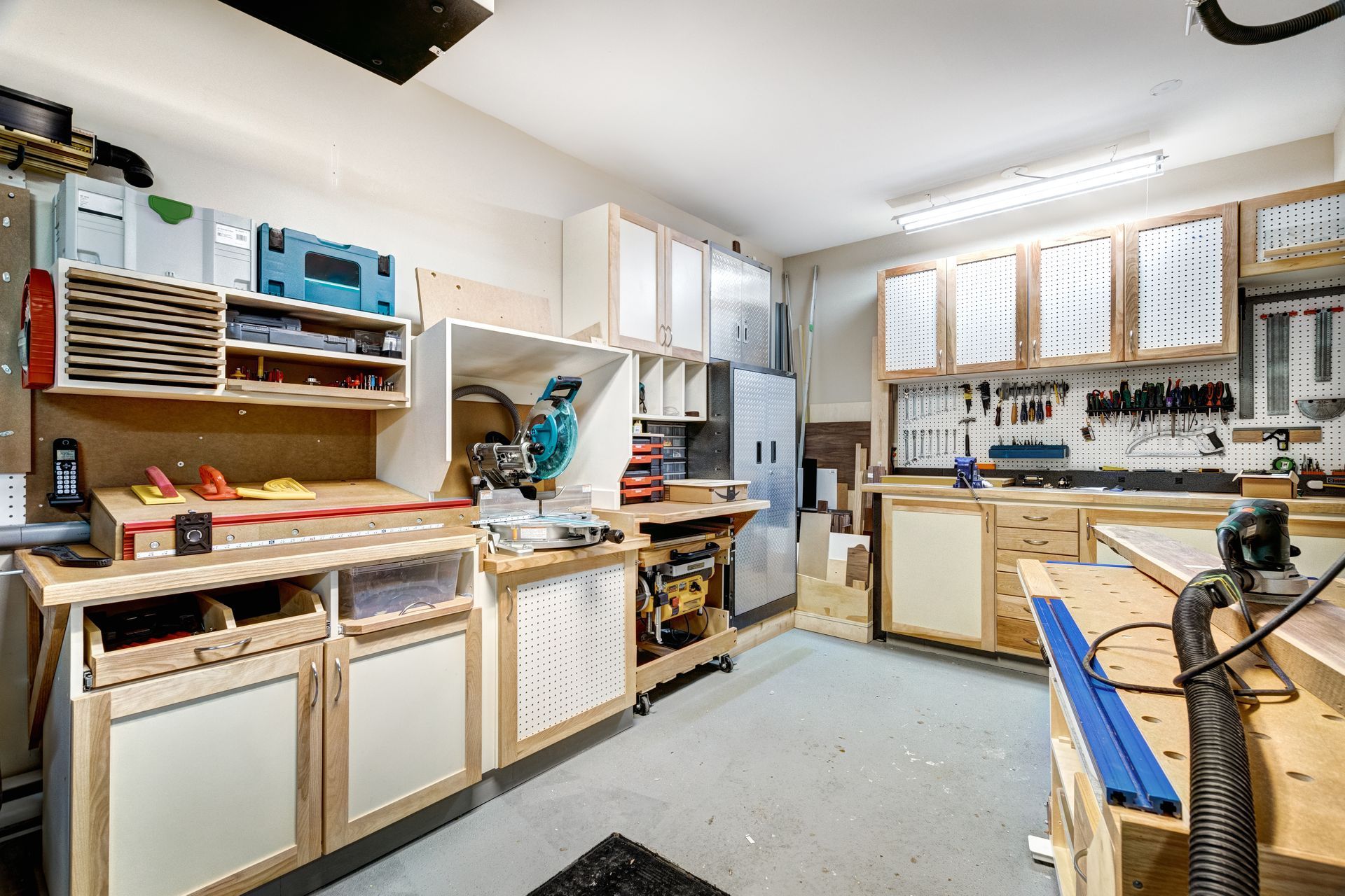 Woodworking garage with workbenches, tools, and storage cabinets in a well-lit space.