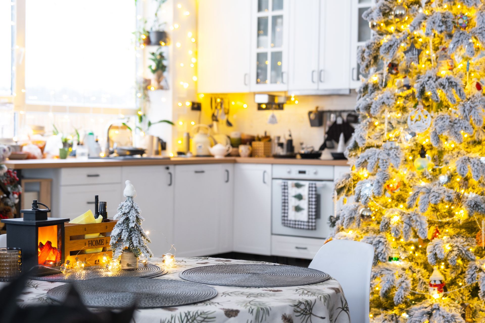 Cozy kitchen decorated for Christmas with a lit tree, table set, and lights strung around.