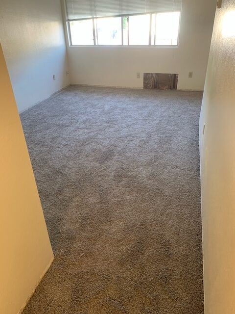 An empty living room with a carpeted floor and a window.