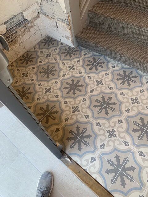 A person is standing on a tiled floor next to stairs.