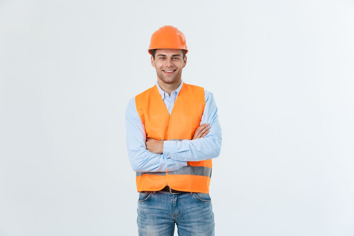 A man wearing a hard hat and an orange vest is standing with his arms crossed.