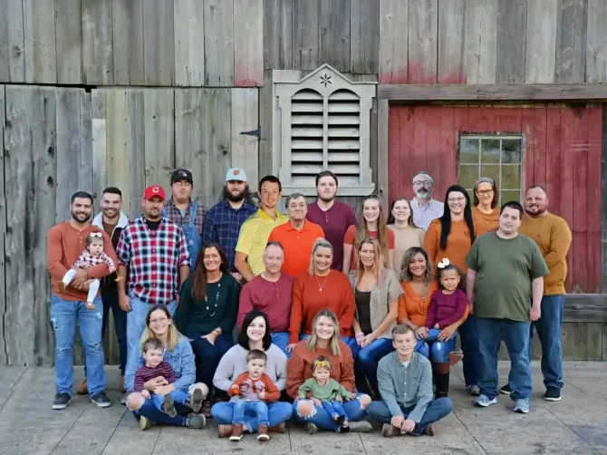 A large family is posing for a picture in front of a barn.
