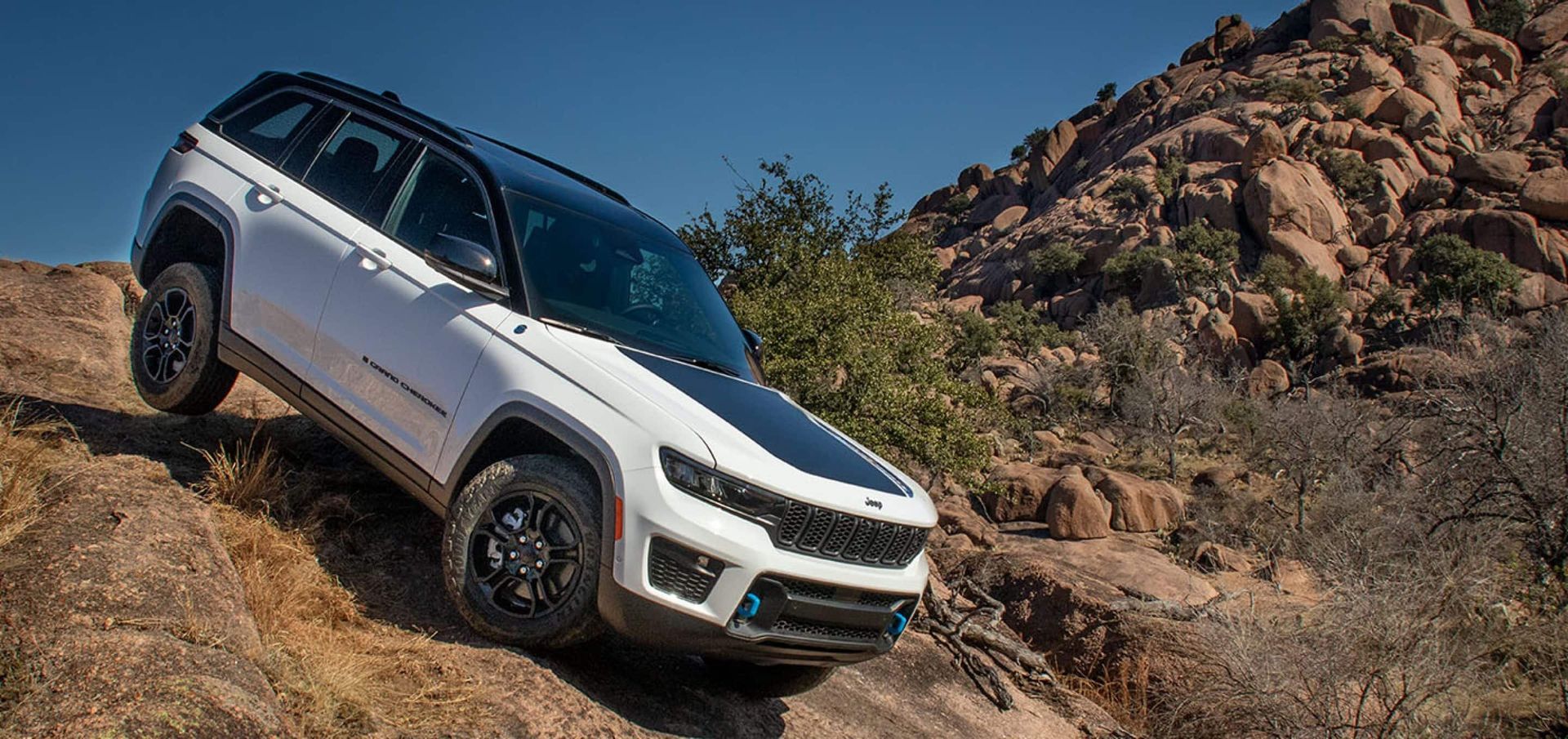 A white jeep grand cherokee is driving down a rocky hill.