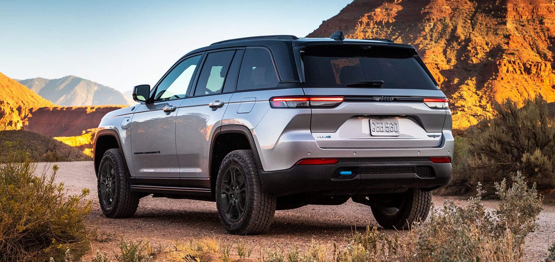 A silver jeep grand cherokee is parked on a dirt road in the desert.