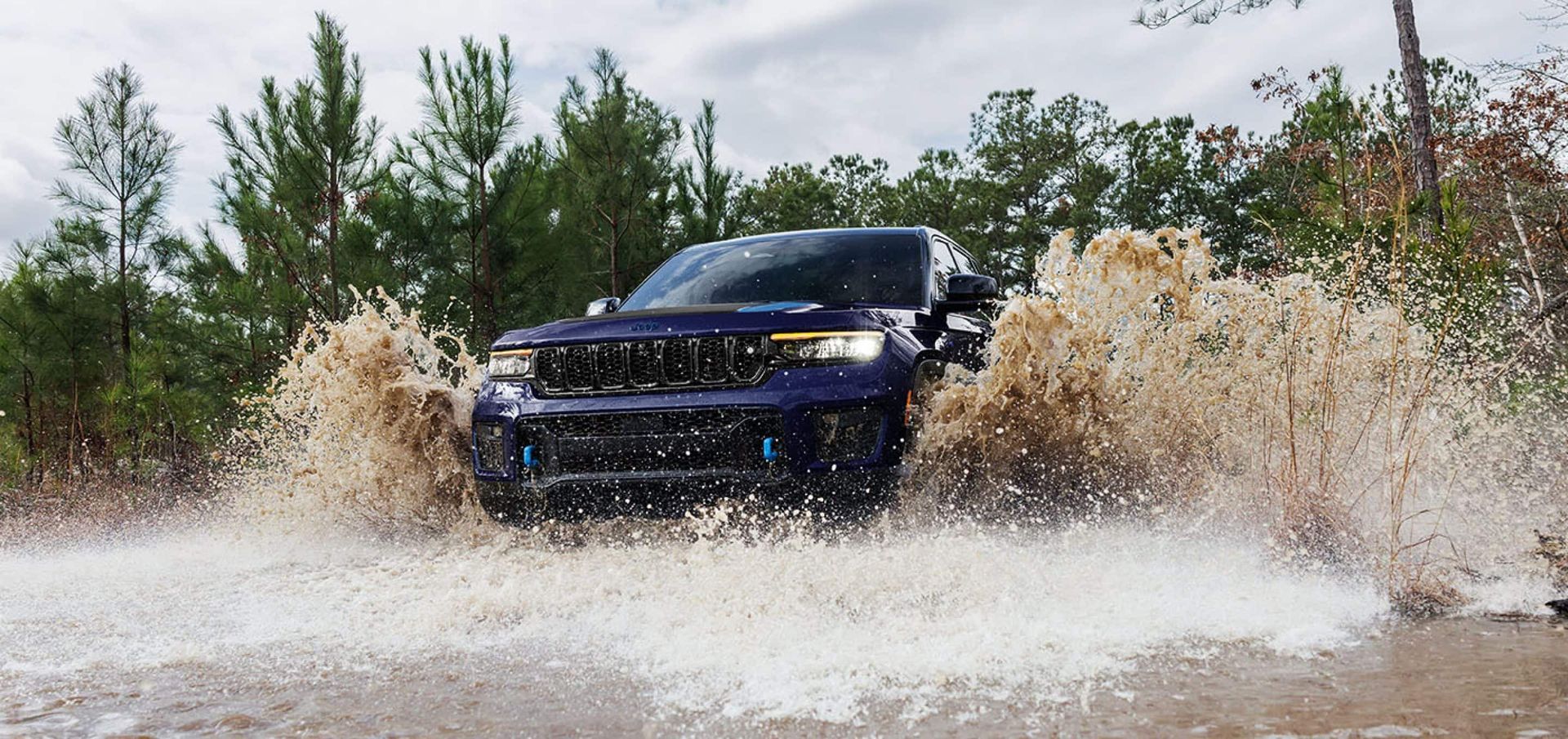 A blue jeep is driving through a puddle of water.