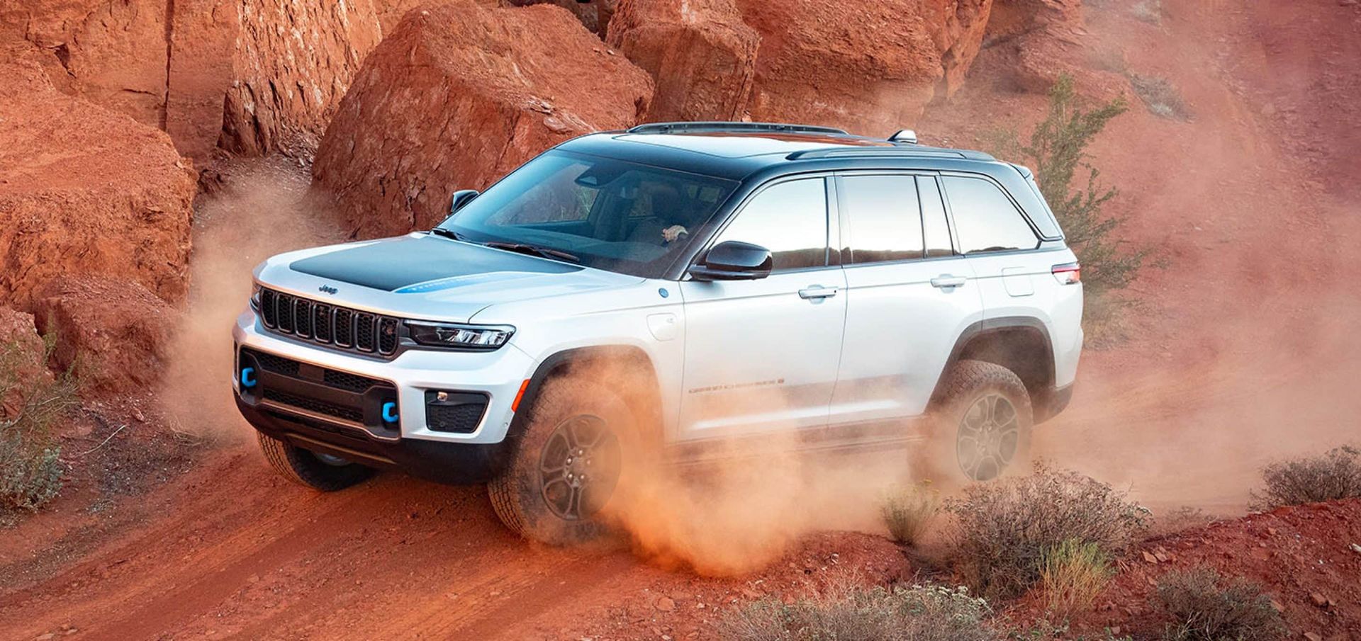 A white jeep grand cherokee is driving down a dirt road.