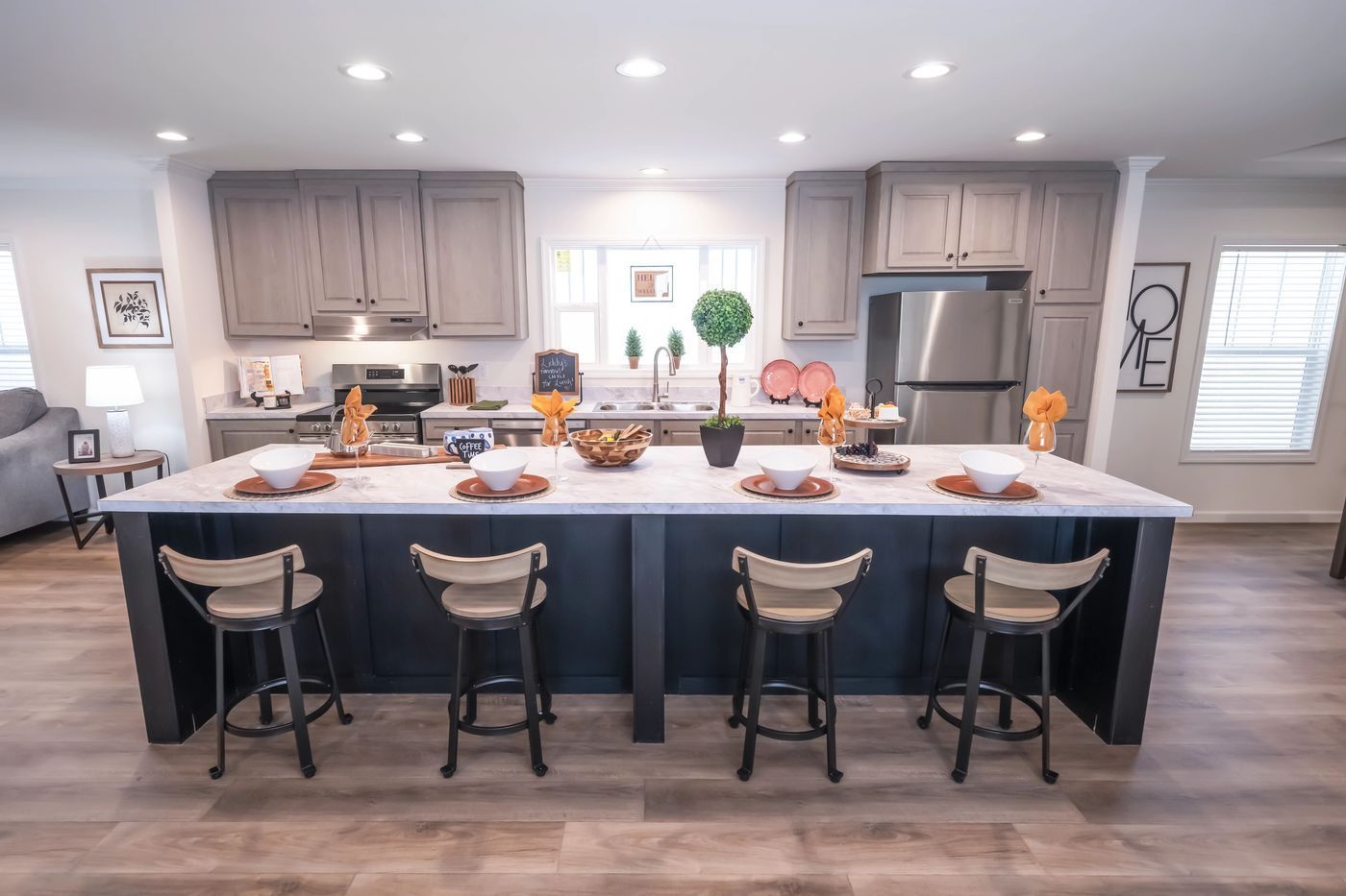 Modern kitchen with a large island, gray cabinets, stainless steel appliances, and four bar stools.