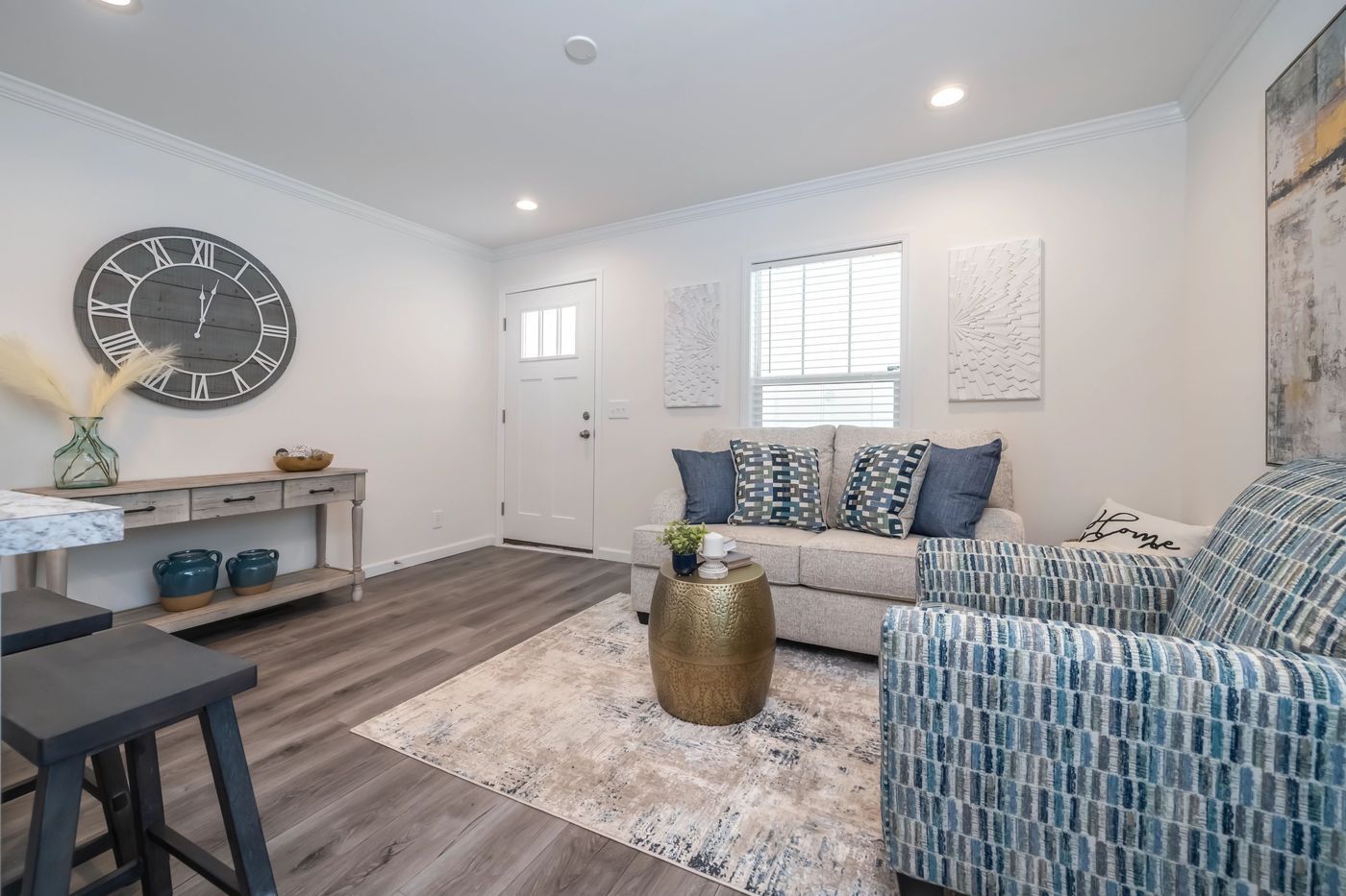 Living room with gray wood floors, neutral walls, blue and white accents, and a gold coffee table.