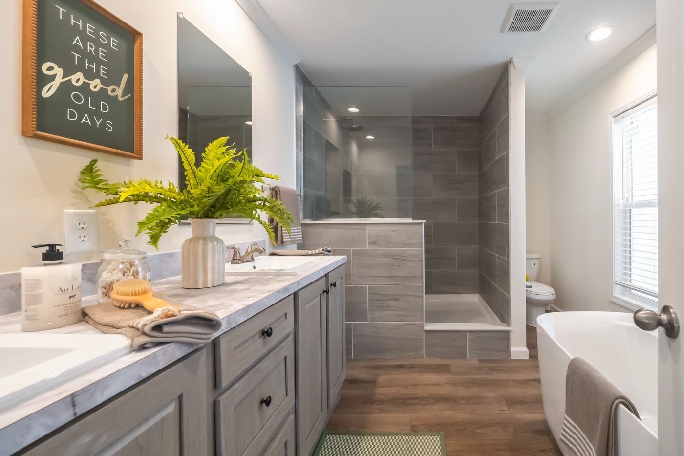 Bathroom with gray cabinetry, a walk-in shower, freestanding tub, and a sign that says 
