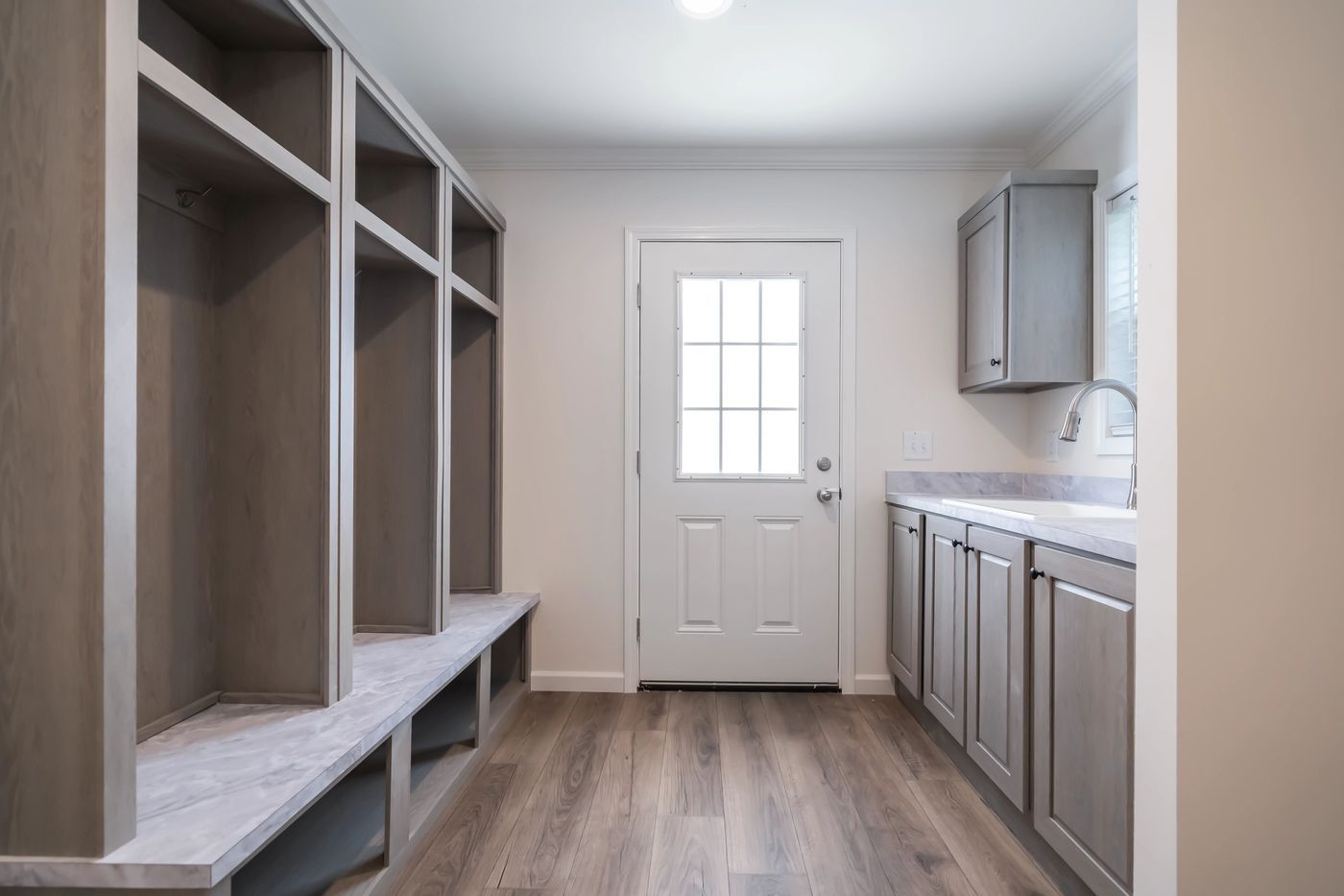 mudroom with gray cabinets and cubbies, white door, and wood-look flooring.