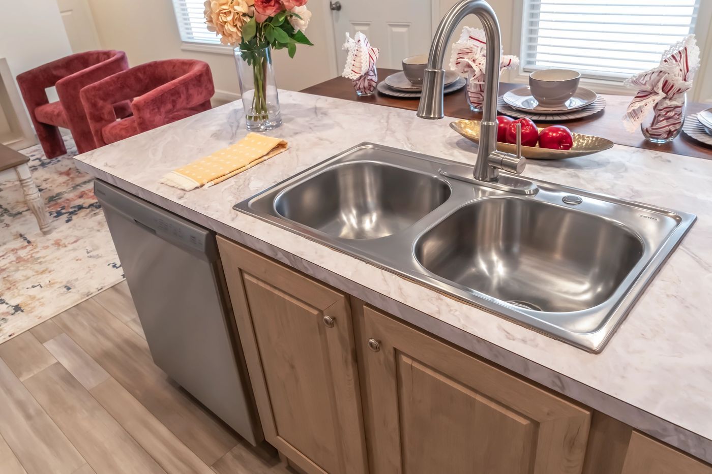 Kitchen island with double sink, dishwasher, light wood cabinets, and countertop.