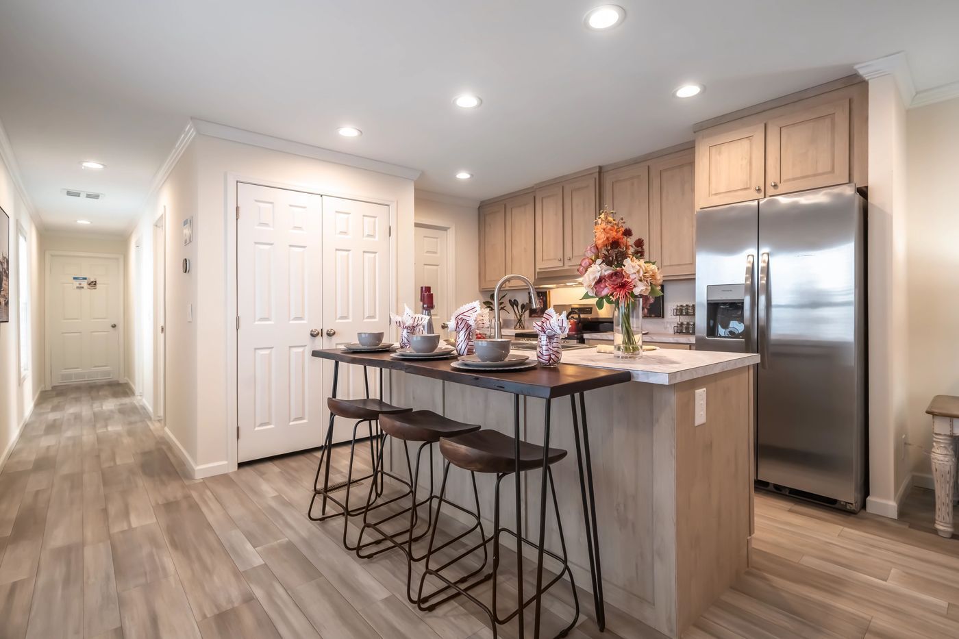 Kitchen with island, bar stools, and stainless steel refrigerator. Light wood cabinets and floors.