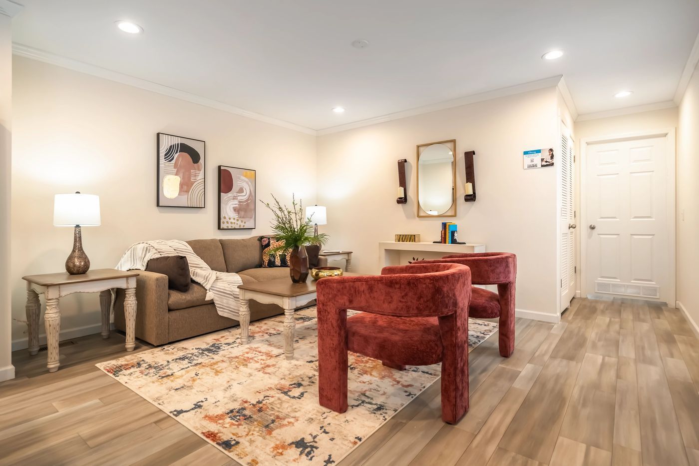 Living room with a brown sofa, two red chairs, artwork, and a rug.