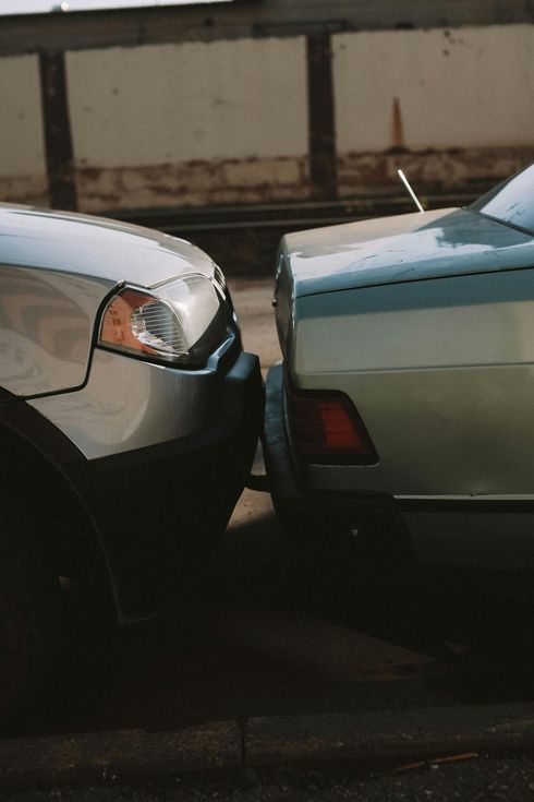 Two cars are parked next to each other and one has a broken bumper