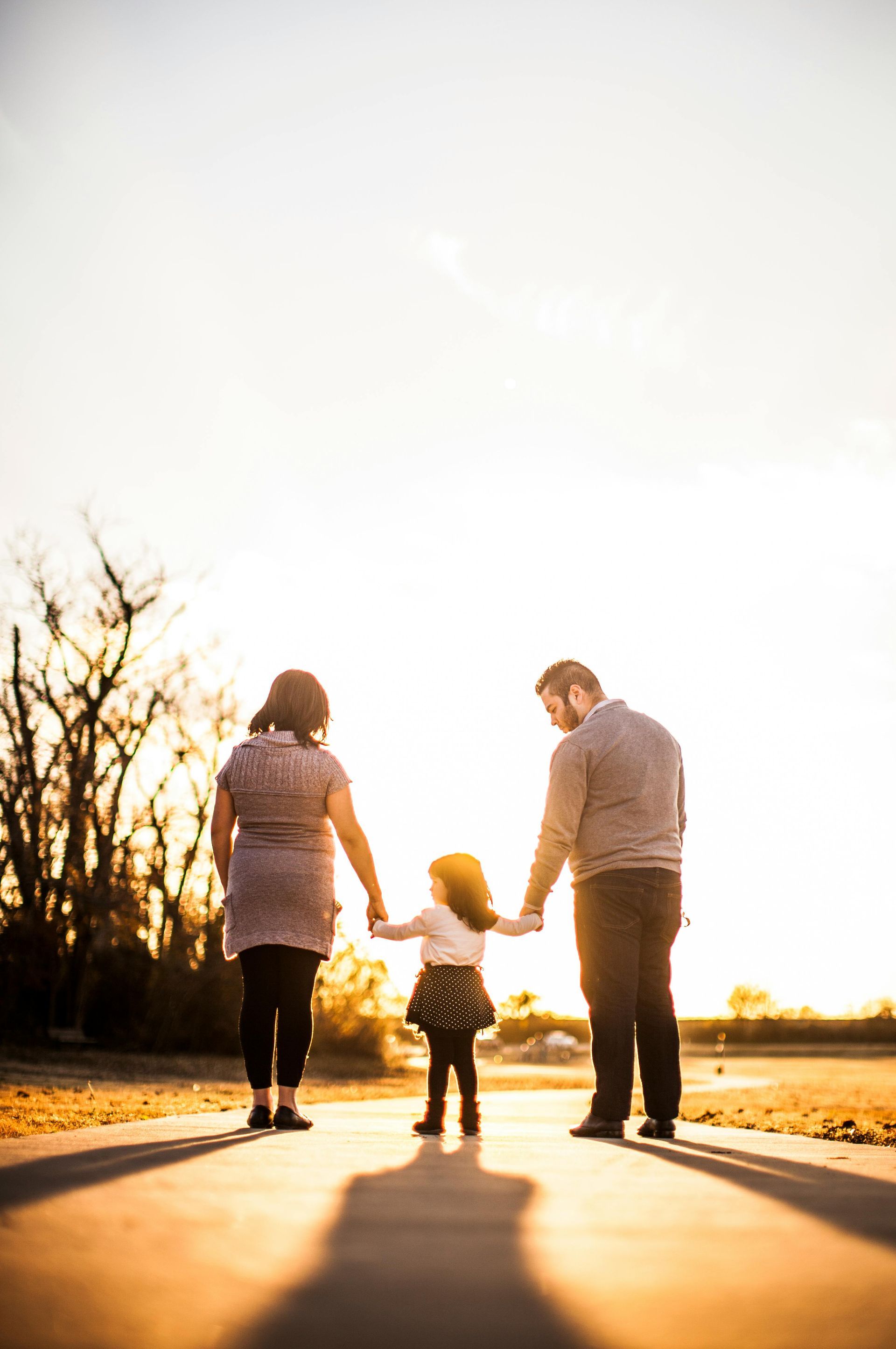 A family is walking down a sidewalk holding hands at sunset.