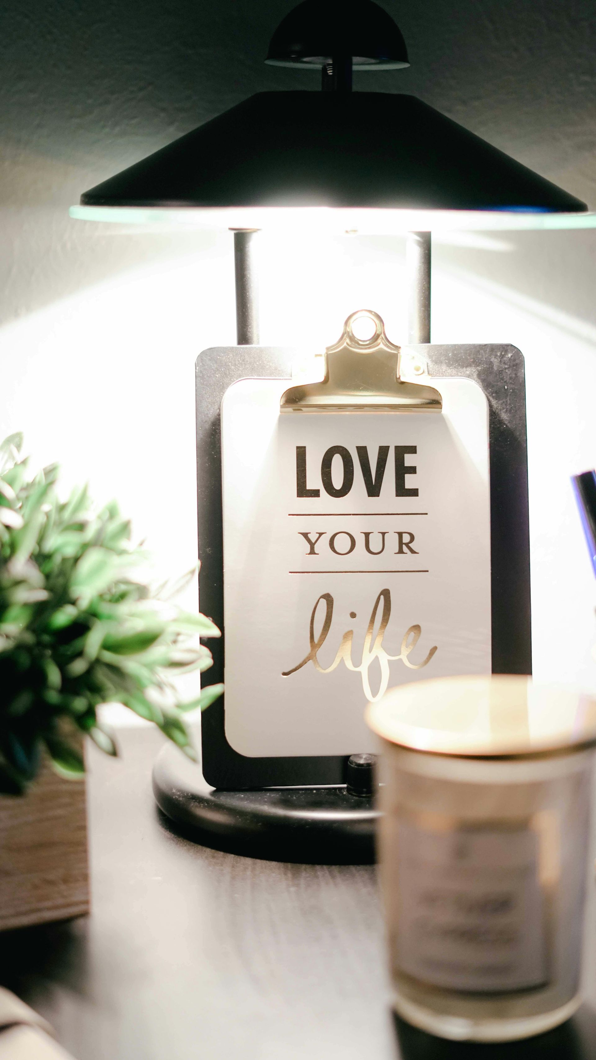 A lamp is sitting on a table next to a clipboard that says `` love your life ''.