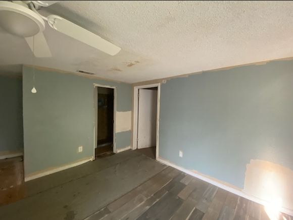 Room with light blue walls, damaged floorboards, and two doorways; ceiling fan visible.
