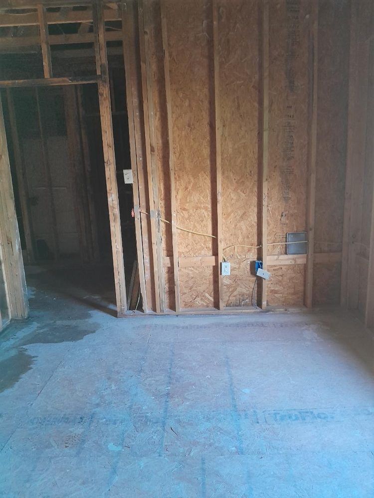 Interior of unfinished room, wood framing with electrical outlets, concrete floor.