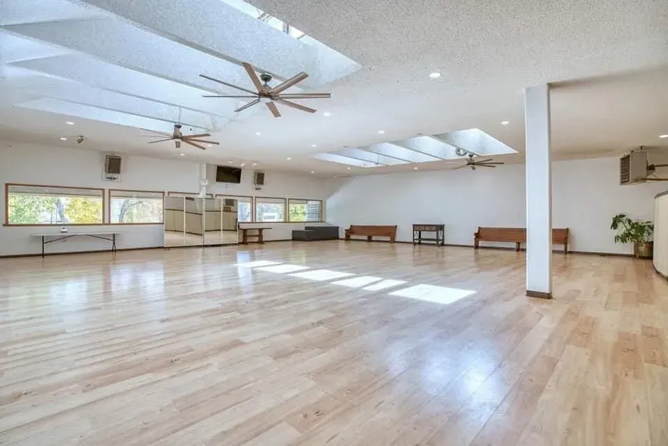 Empty, sunlit room with light wood floors, skylights, and windows. Brown benches line one wall.