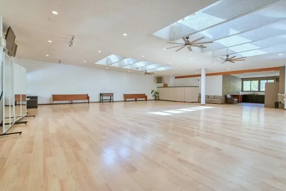 Empty dance studio with hardwood floor, mirrors, skylights, benches, and ceiling fans.