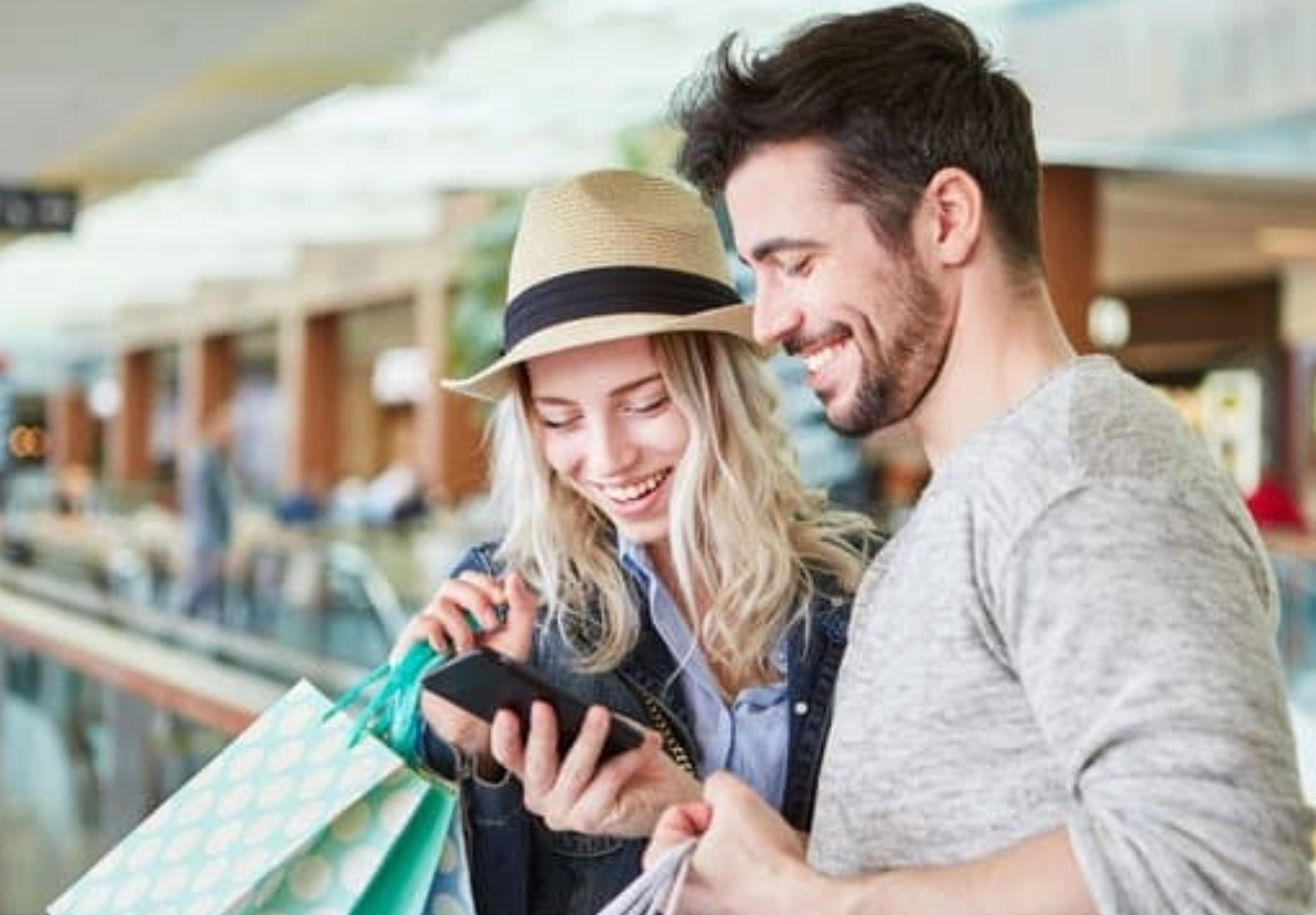 A man and a woman are shopping in a mall and looking at a cell phone.