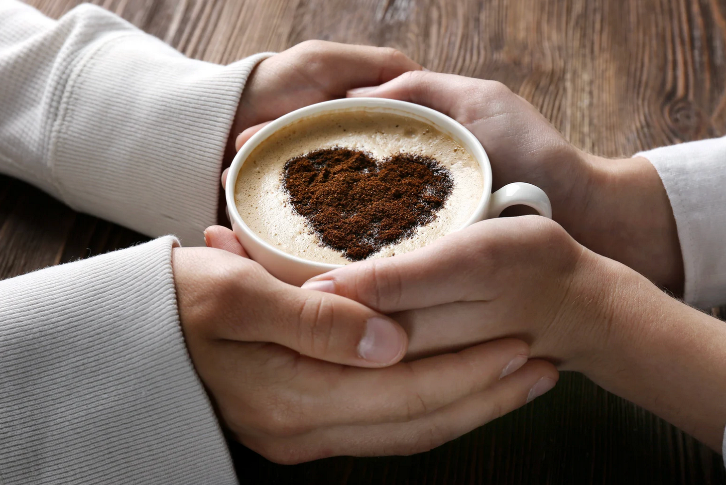 Two people are holding a cup of coffee with a heart drawn on it.