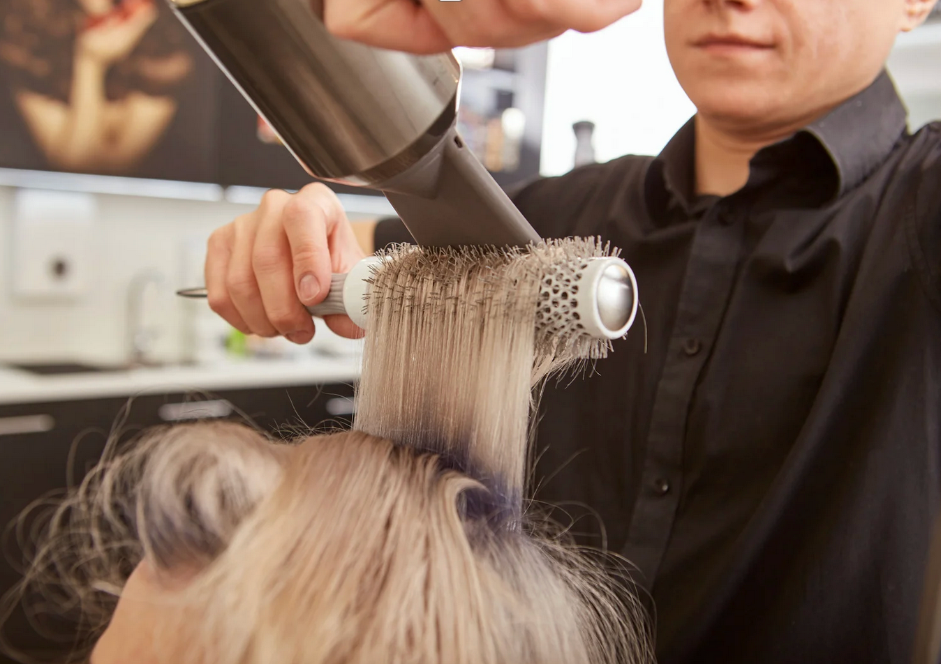 A man is blow drying a woman 's hair with a brush