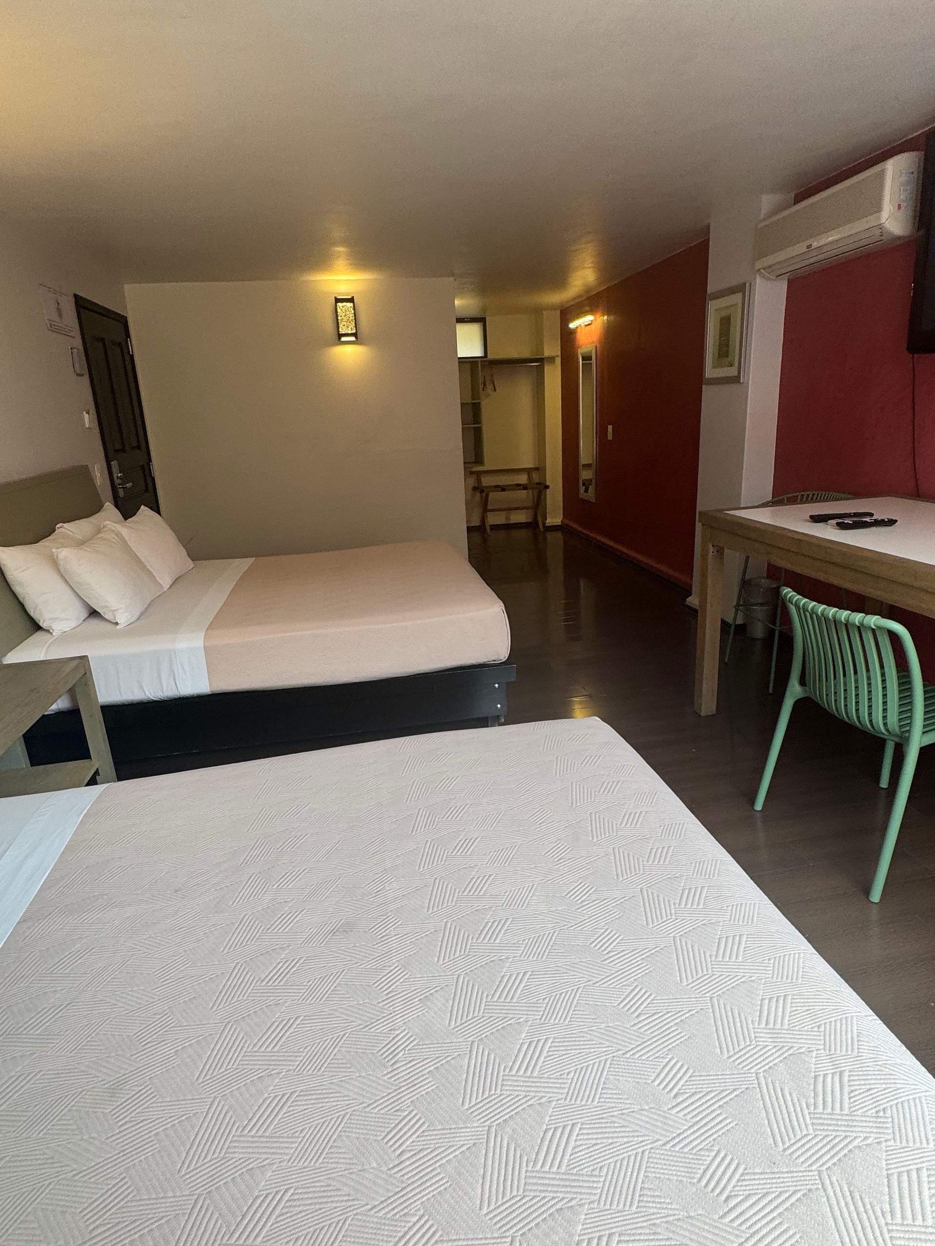 Bedroom with a bed, nightstand, and a patterned wallpaper accent wall, reflected in a framed mirror.