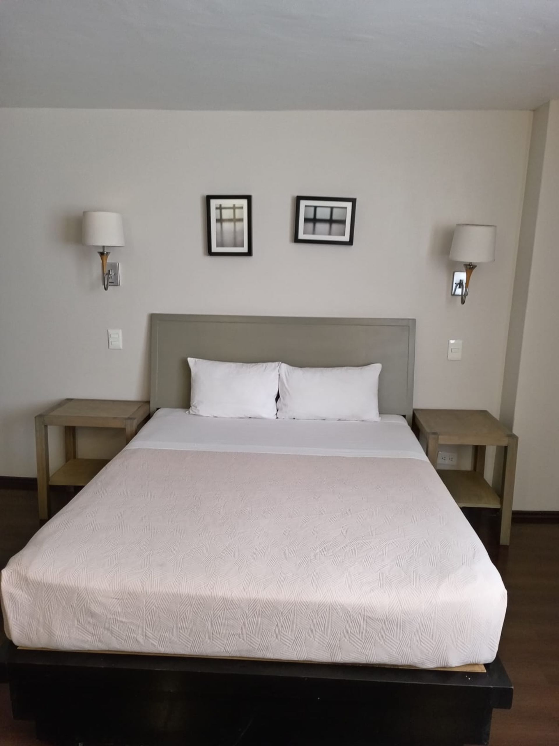 A hotel bedroom with a large bed, a bench at the foot, and a large window with curtains.