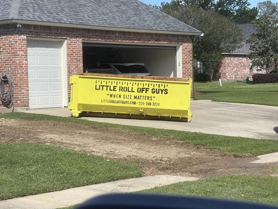 A yellow dumpster is parked in front of a garage.